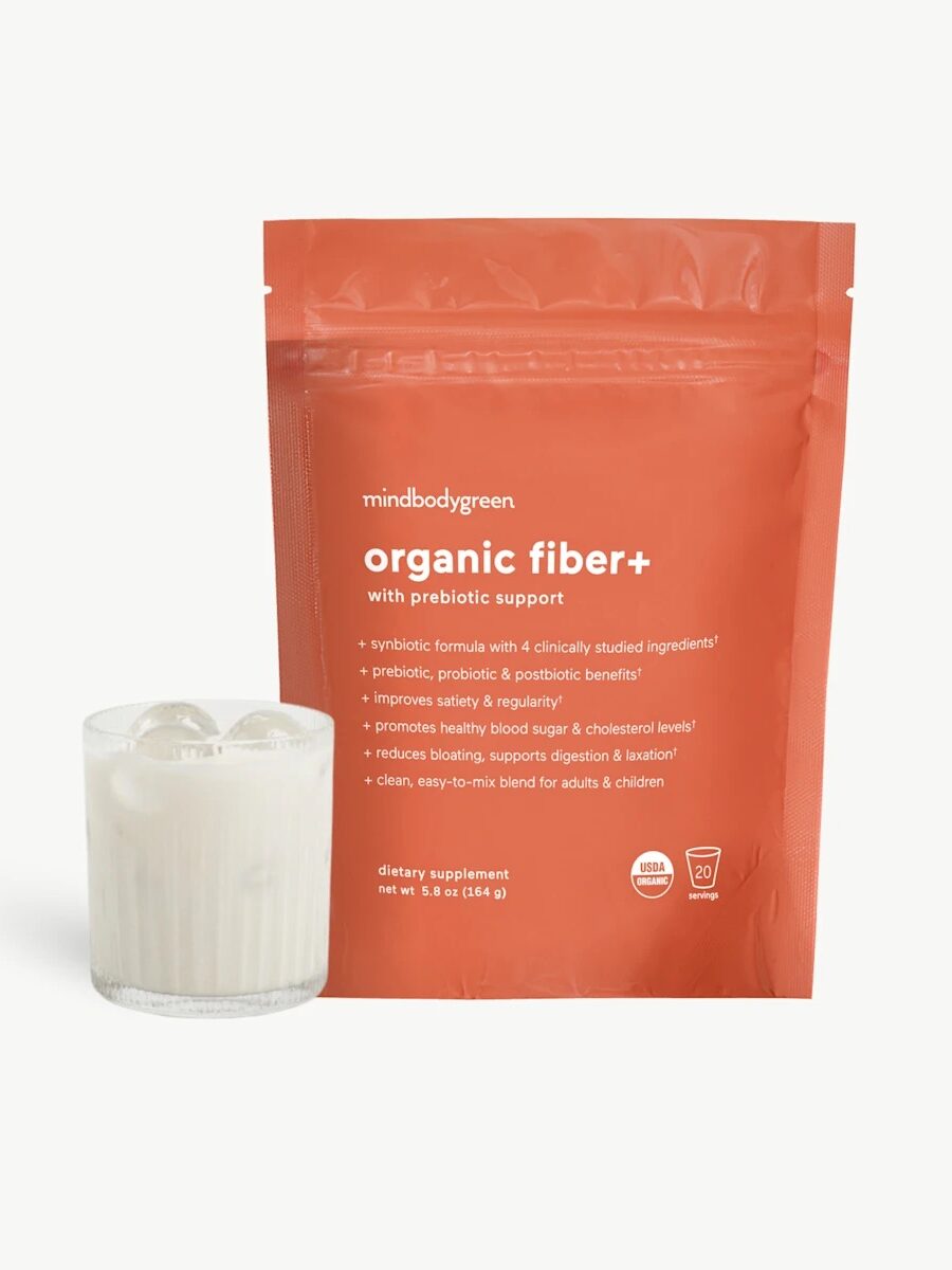 A glass of milk with ice sits next to a red package labeled "organic fiber+ with prebiotic support" dietary supplement by mindbodygreen, one of the top fiber supplements for women.