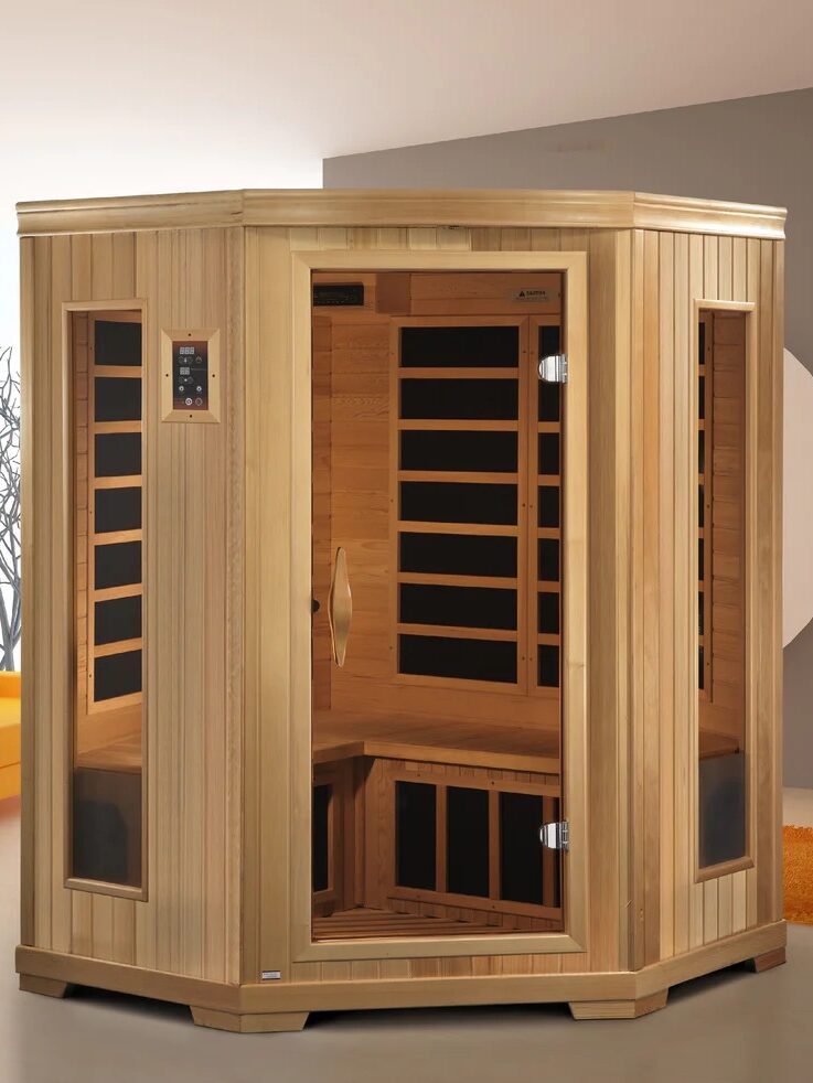 A modern wooden infrared sauna with glass doors and interior seating is placed in a contemporary living room with a yellow sofa and orange rug.
