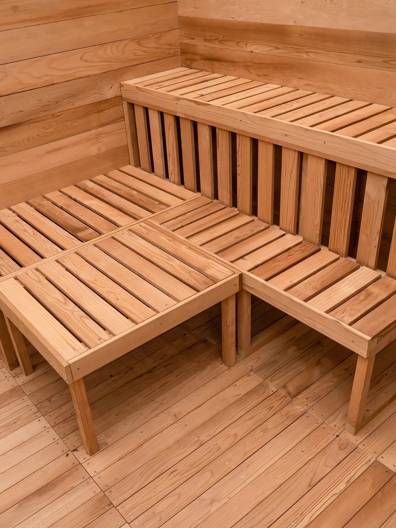 Wooden slatted benches arranged in an L-shape with a matching low table, set against wooden paneled walls and flooring.