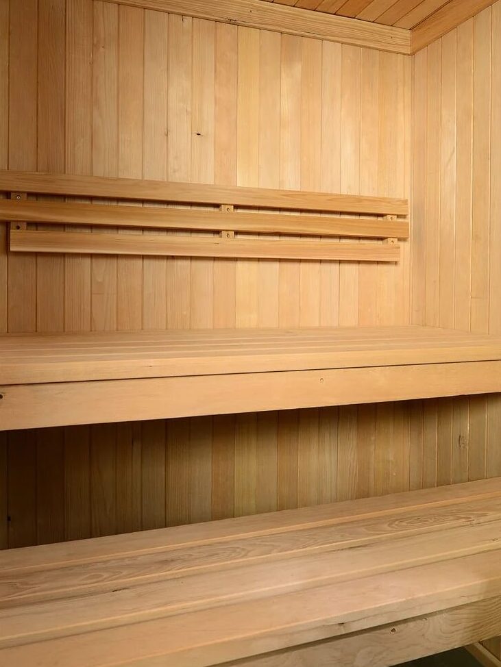 Interior of a wooden sauna with two tiered benches and a Harvia heater in the corner.