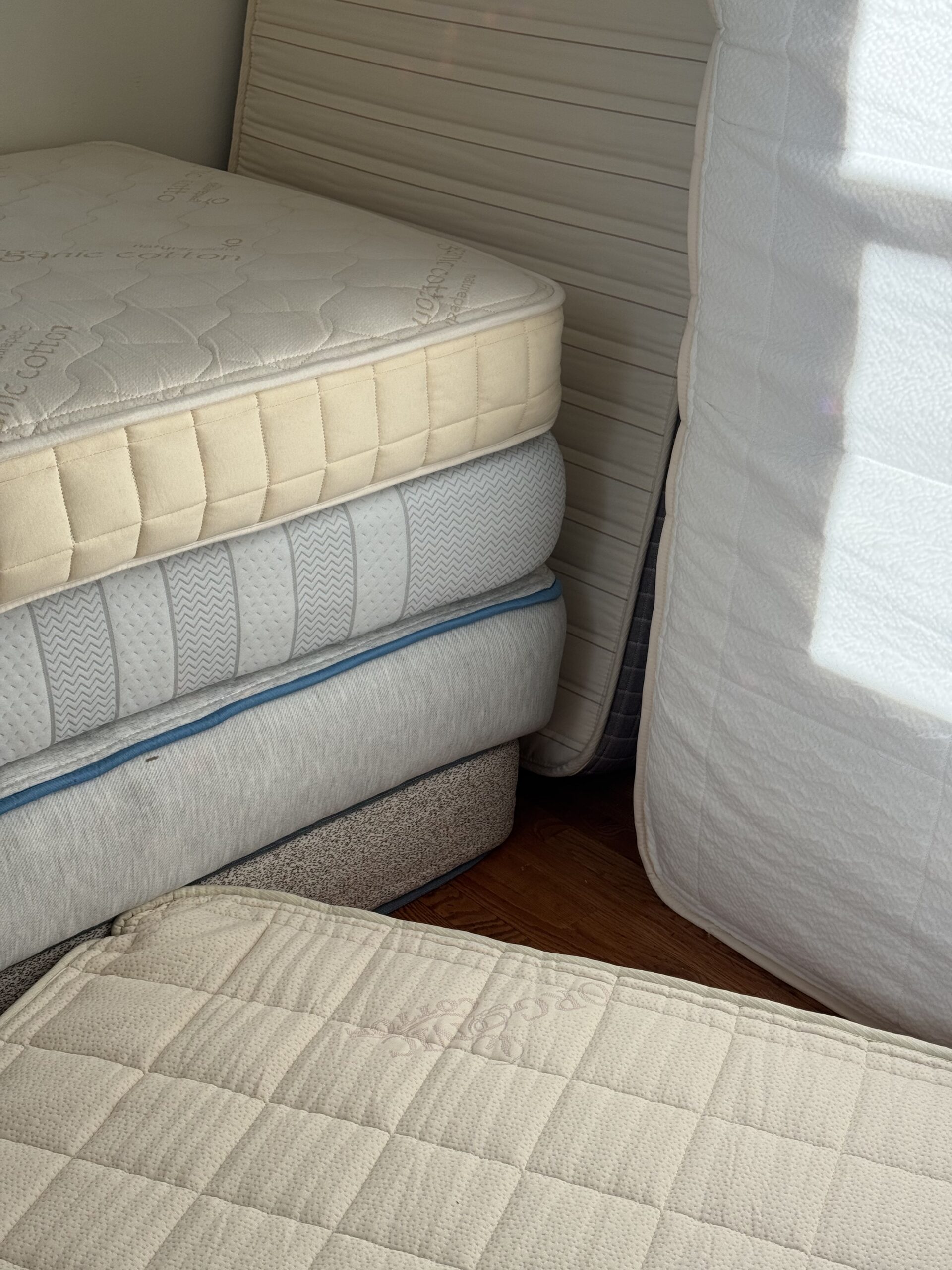A stack of three mattresses with a fourth mattress leaning against a wall and another resting in the foreground.