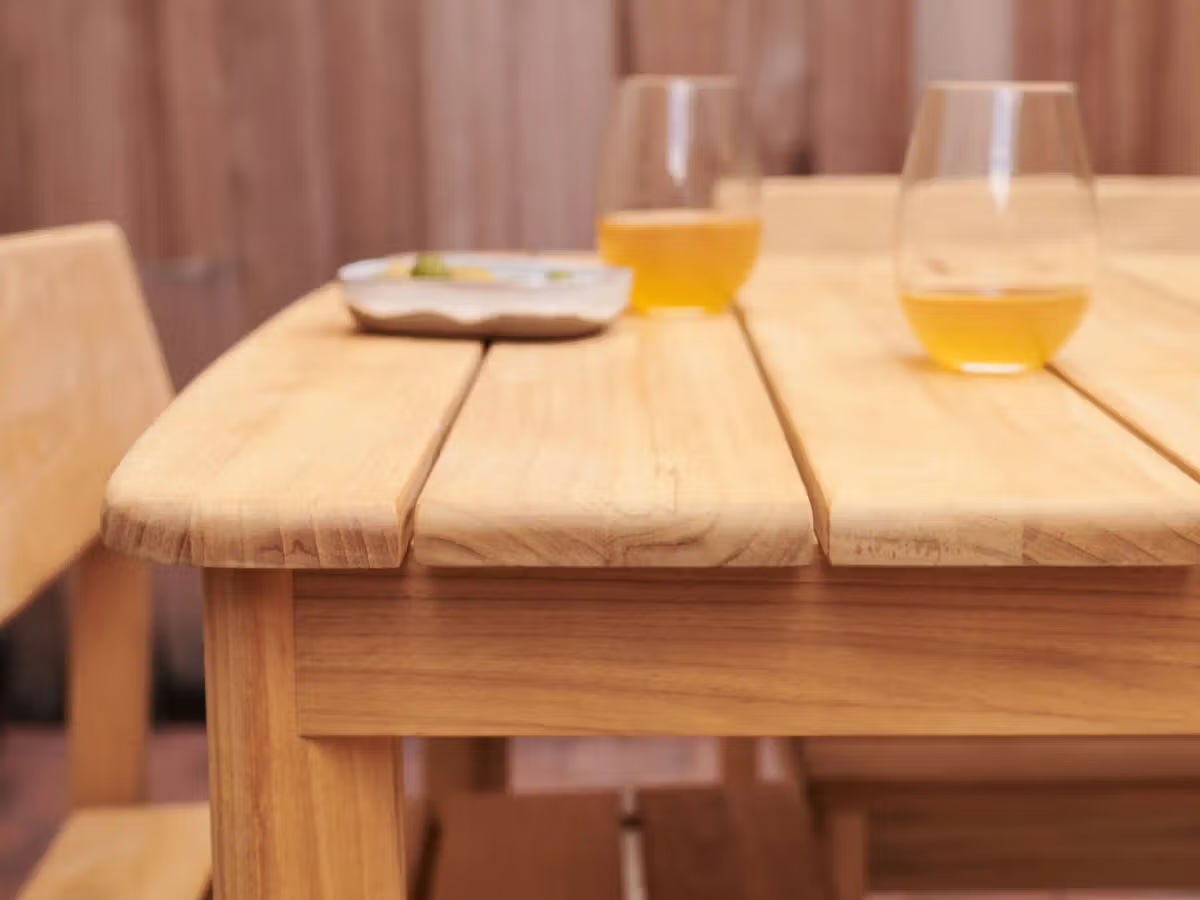 A wooden table with two glasses of orange liquid and a small dish, next to a matching wooden chair.