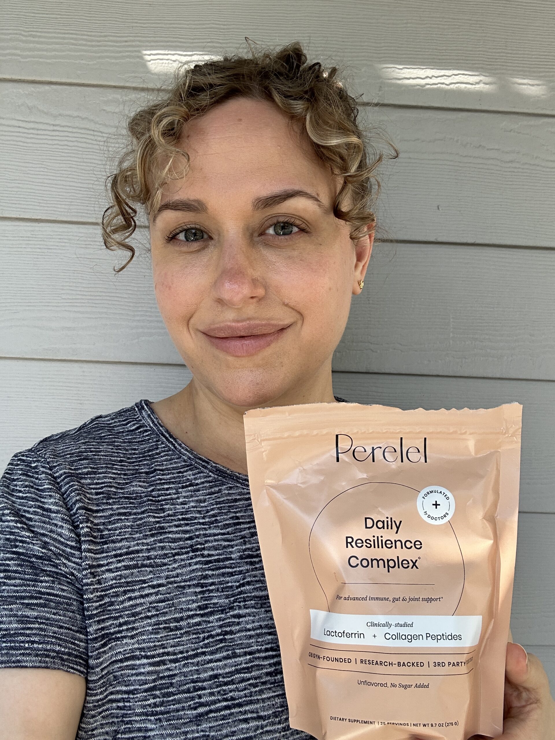 A person holding a package of Perelel Daily Resilience Complex supplement in front of a light-colored wall.