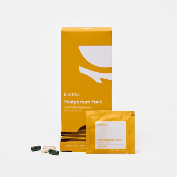 A yellow box labeled "Postpartum Pack" by bird&be, with a single supplement packet and several capsules displayed in front of it.