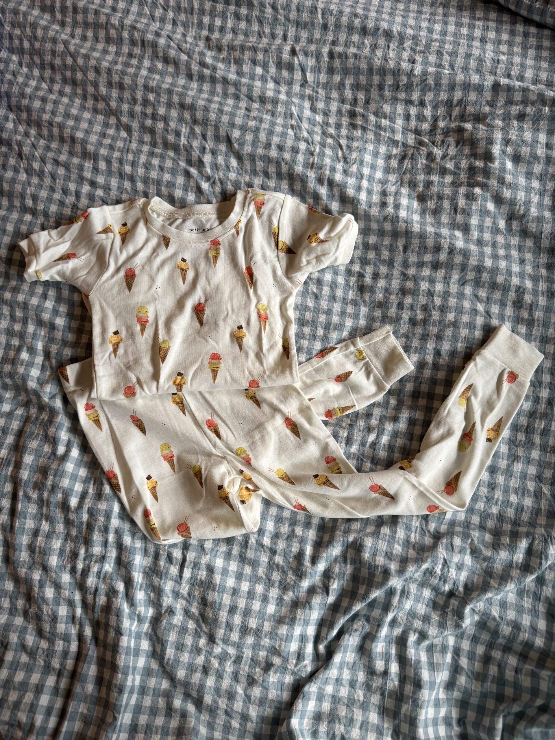 A matching short-sleeve shirt and pants set with an ice cream cone print, laid out on a blue and white checkered fabric background.