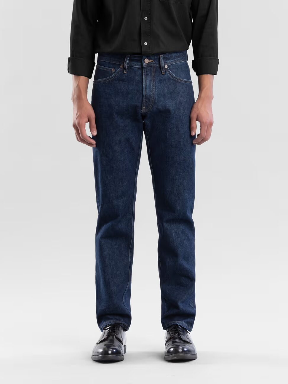 A person wearing a black shirt, blue straight-leg jeans, and black shoes stands against a plain light background.
