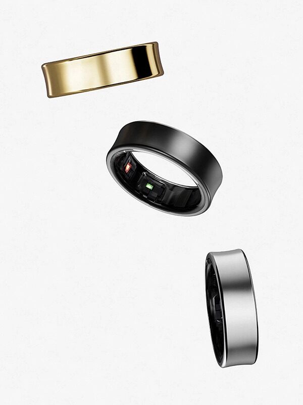 Three rings are shown floating; two have a metallic finish in silver and gold, while the third reveals electronic sensors inside, indicating a smart ring design.