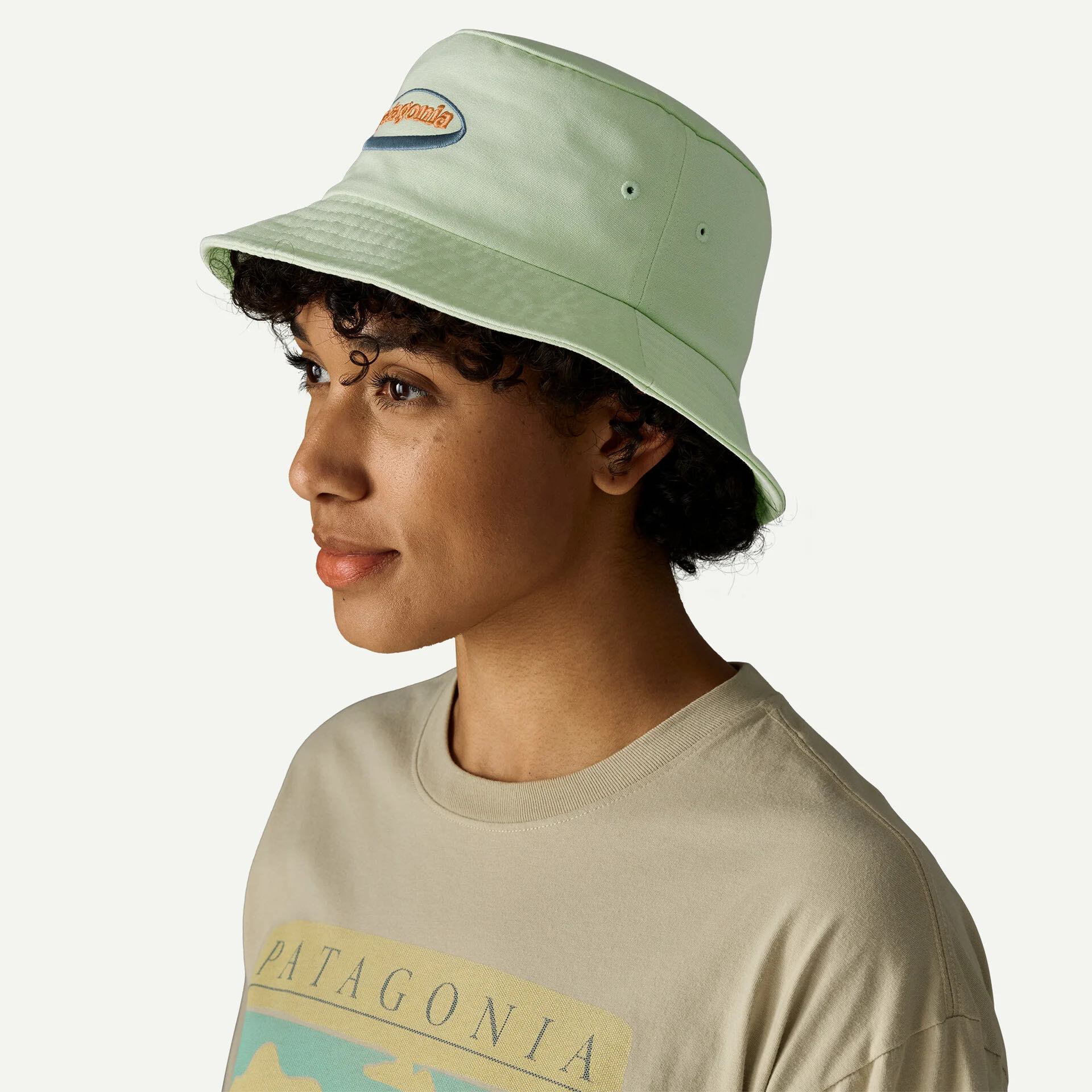 Person wearing a light green bucket hat and a beige Patagonia t-shirt, looking to the side against a plain background.