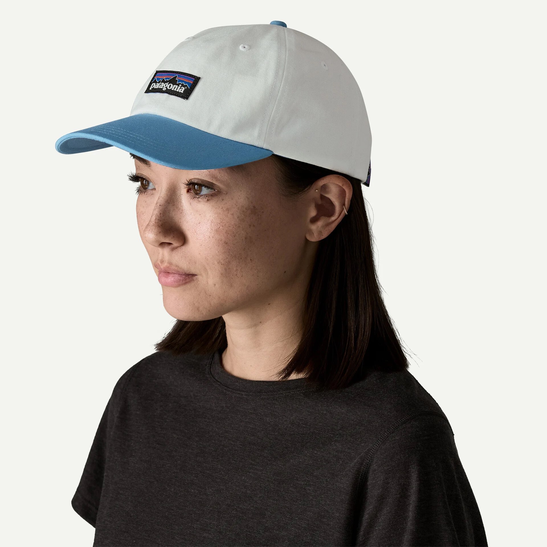 Woman wearing a white and blue baseball cap with “Patagonia” logo and a dark t-shirt, shown against a plain light background.
