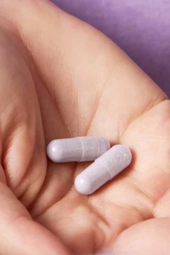 A hand holding two purple capsules against a purple background.