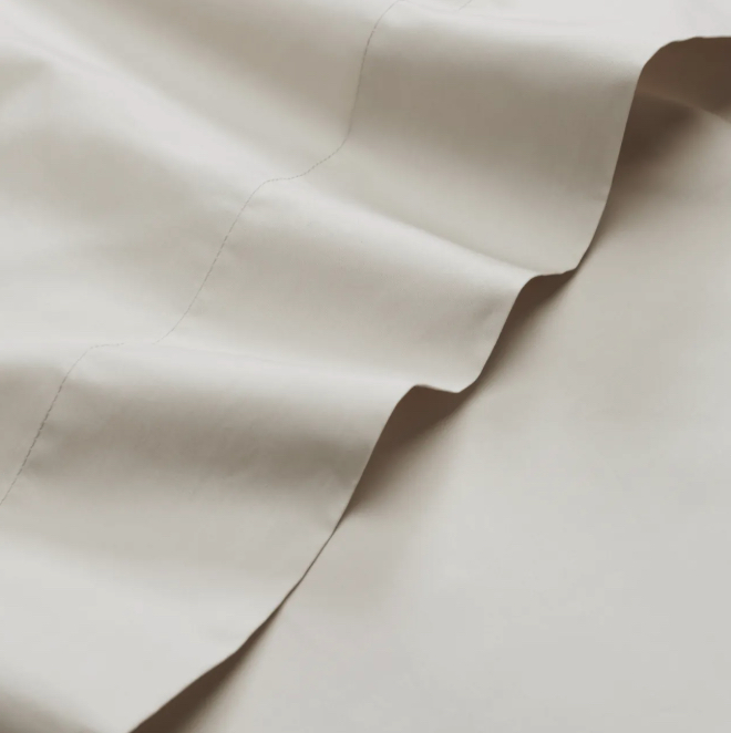 A close-up of a white or off-white fabric, often used for cooling sheets, with visible stitching and gentle folds creating soft shadows.