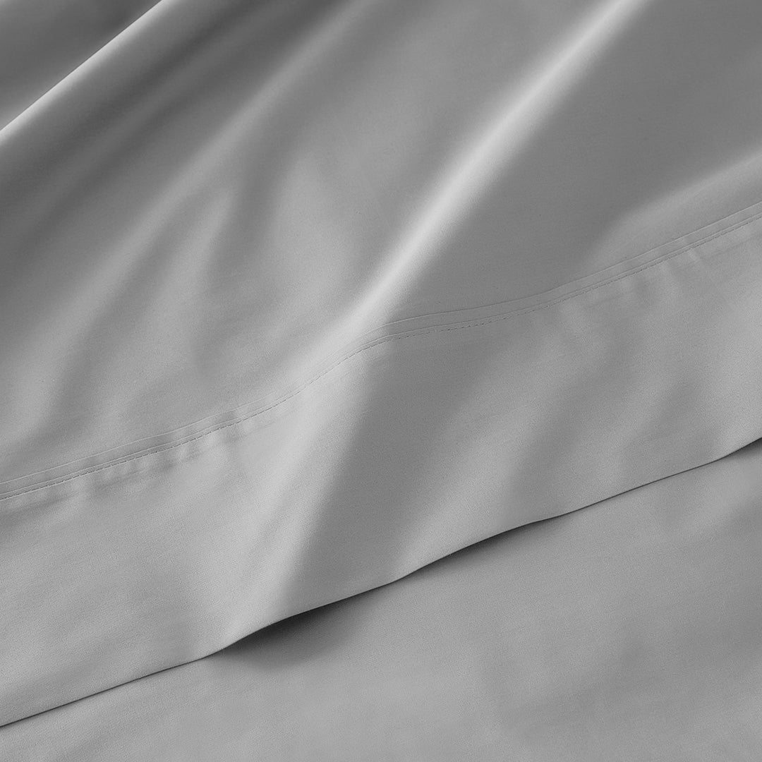 Close-up of smooth, light gray cooling sheets with subtle stitching detail and gentle folds.
