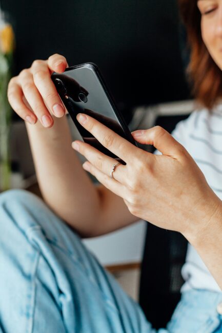 A person wearing a striped shirt and jeans is holding and using a smartphone, with one hand touching the screen.
