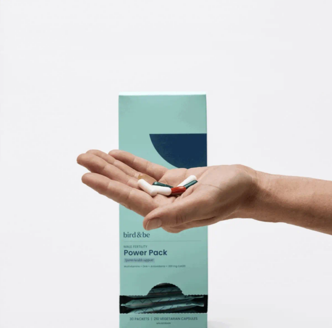 A hand holds several capsules in front of a teal box labeled “Power Pack” by bird&be, a male fertility support supplement.