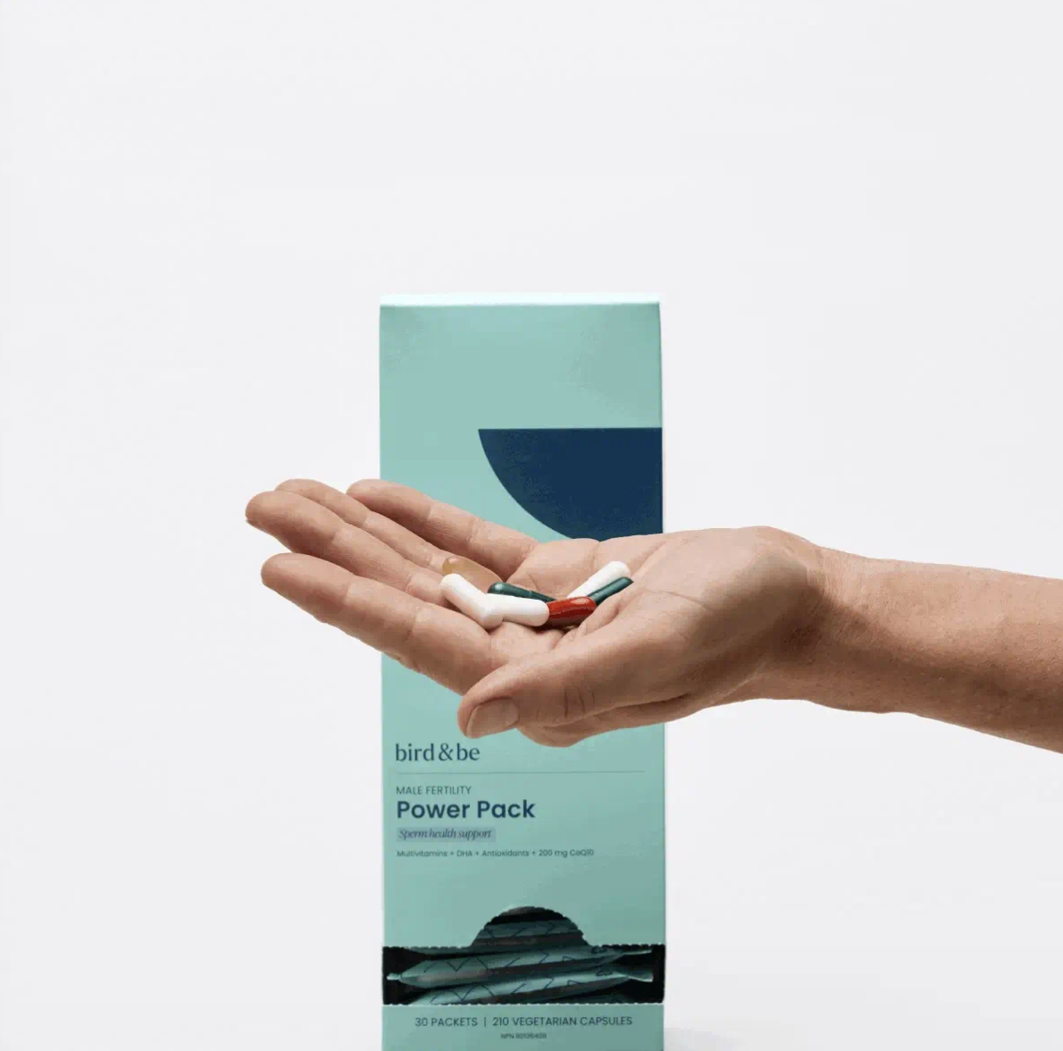 A hand holds several capsules in front of a teal box labeled “Power Pack” by bird&be, a male fertility support supplement.