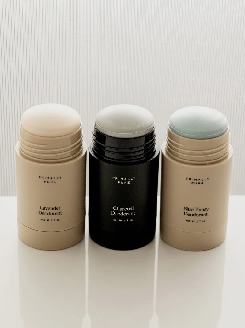 Three opened stick deodorants labeled Lavender, Charcoal, and Blue Tansy are arranged side by side on a light surface against a striped background.