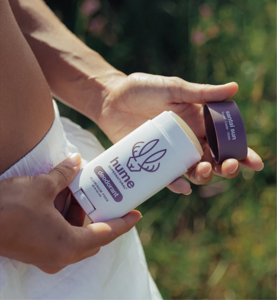 Person holding an open stick of Hume deodorant outdoors, with the deodorant cap in one hand and the stick in the other.
