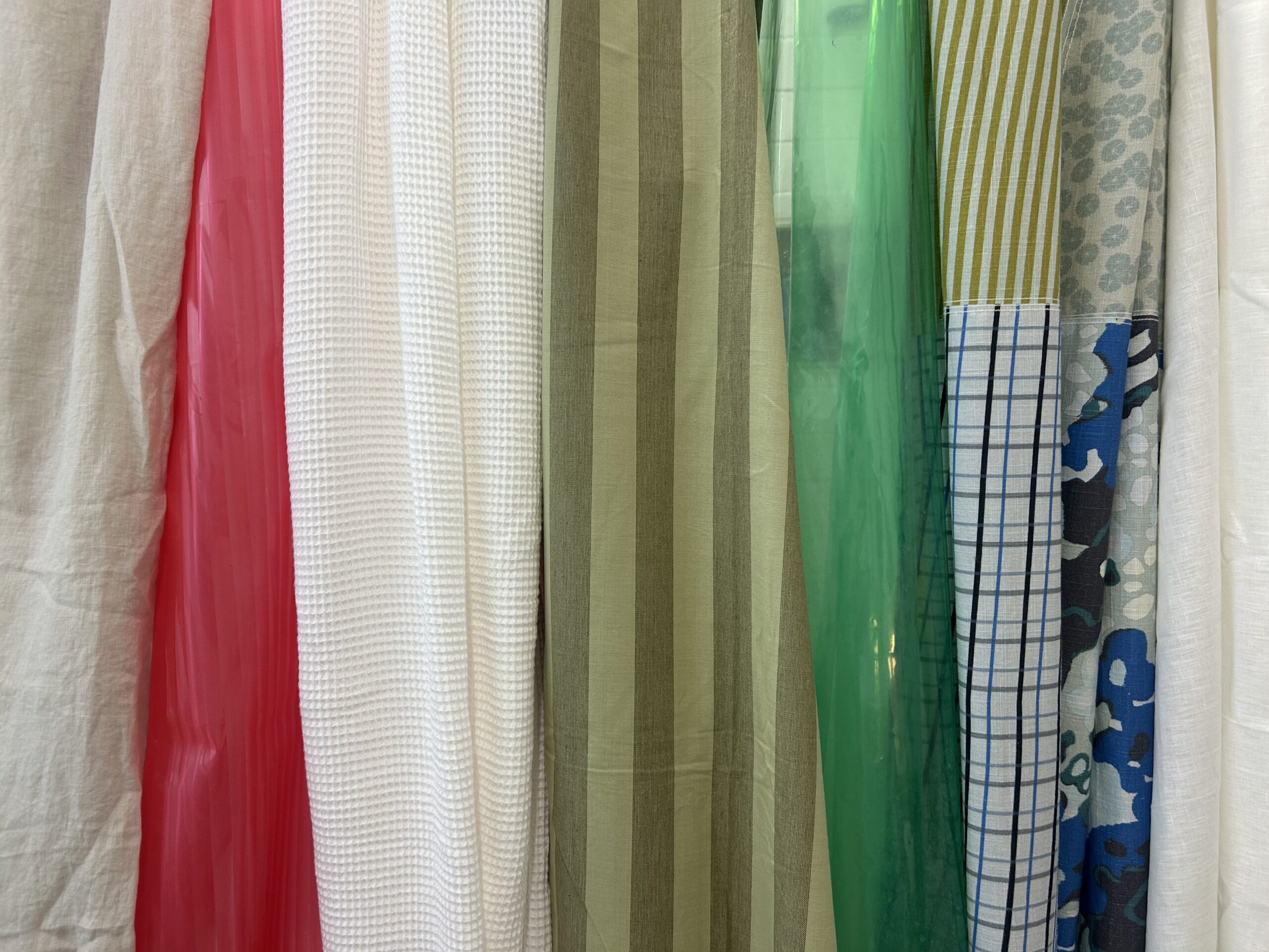 Several long fabric panels hang side by side, featuring a variety of colors, patterns, and textures including solid, striped, checked, and floral designs.