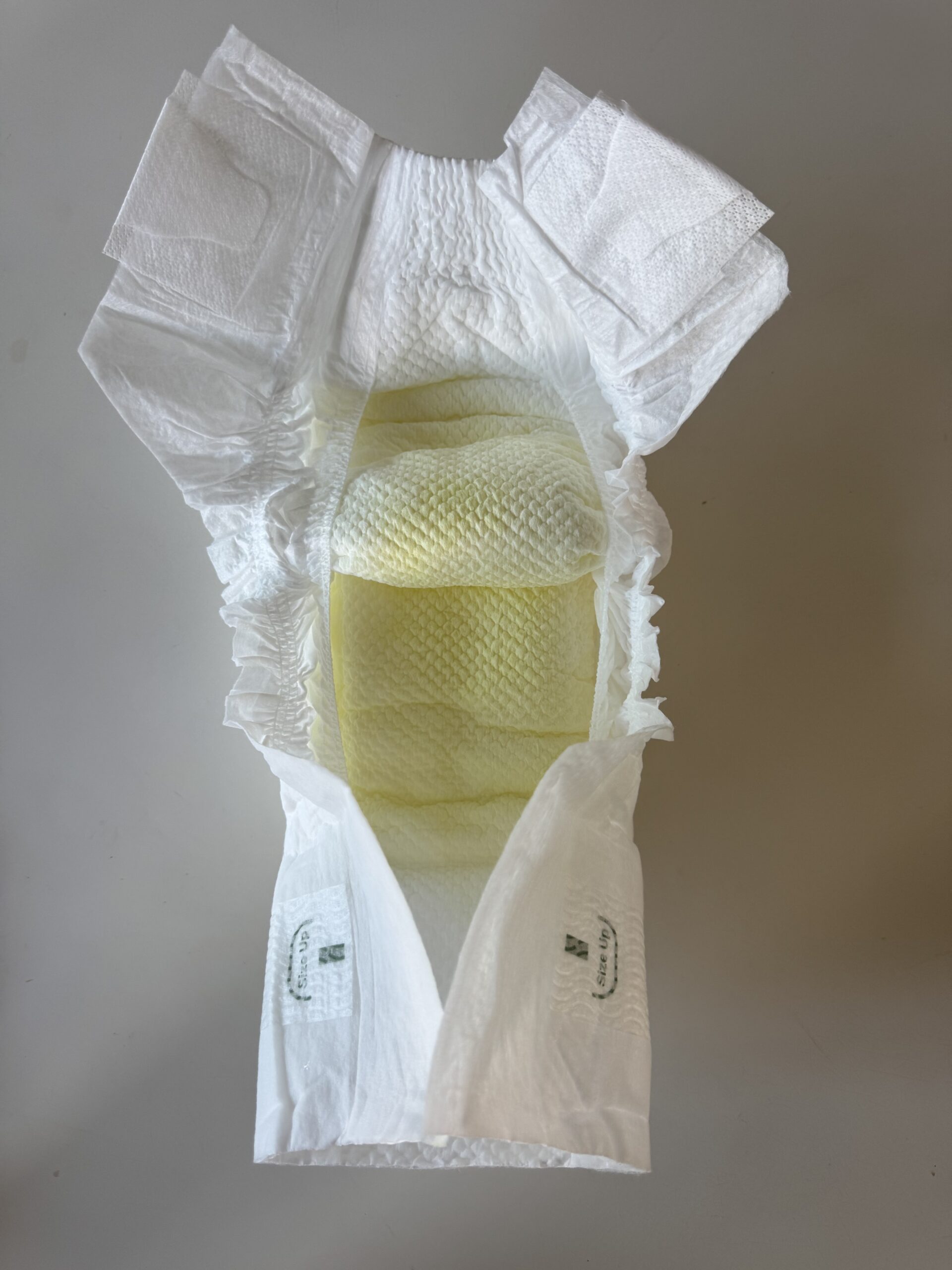 An open disposable diaper shows a yellow stain in the absorbent area, indicating it has been used.