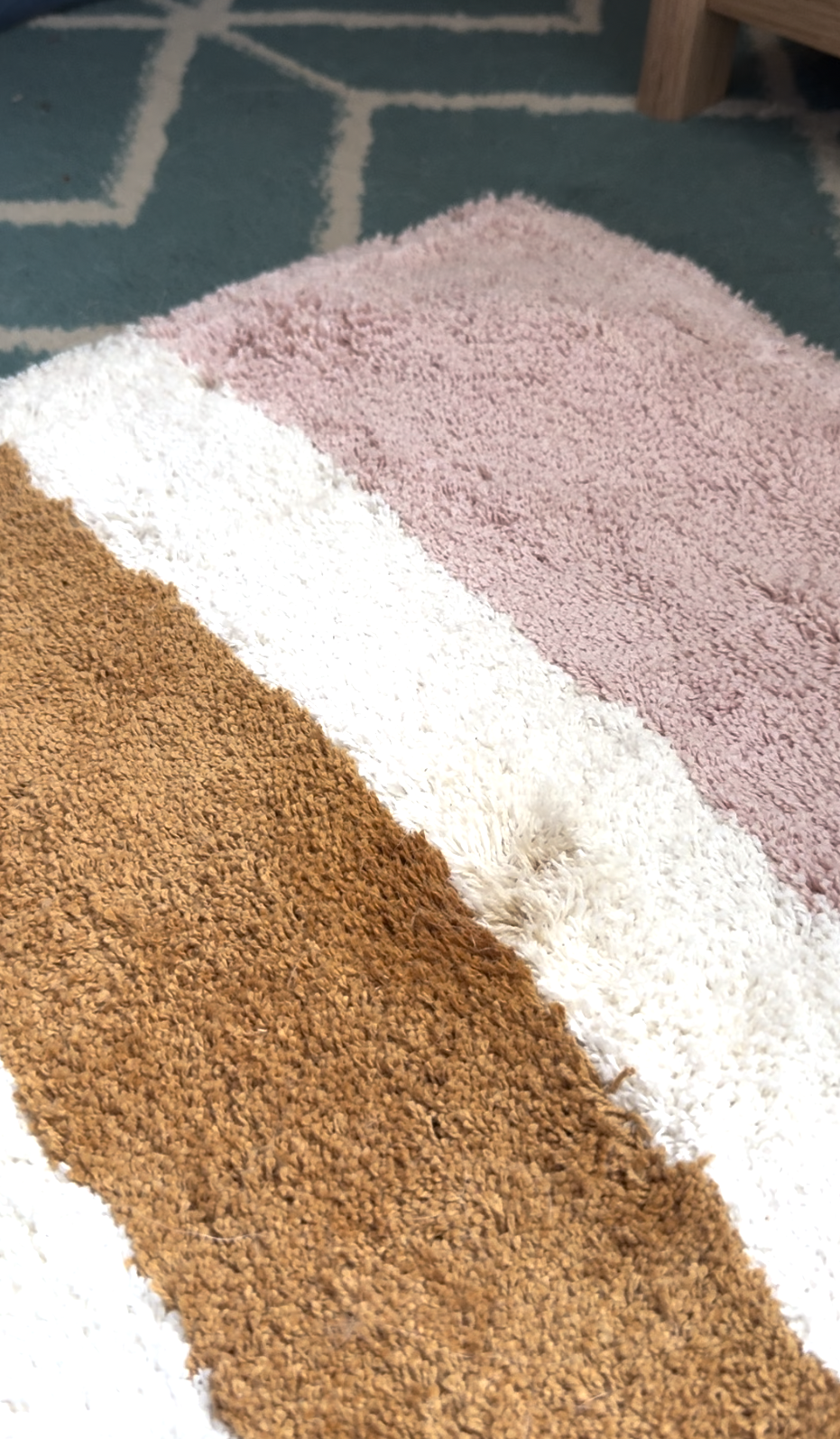 A close-up of a textured rug with brown, white, and pink stripes, placed on top of a teal carpet with white geometric lines.