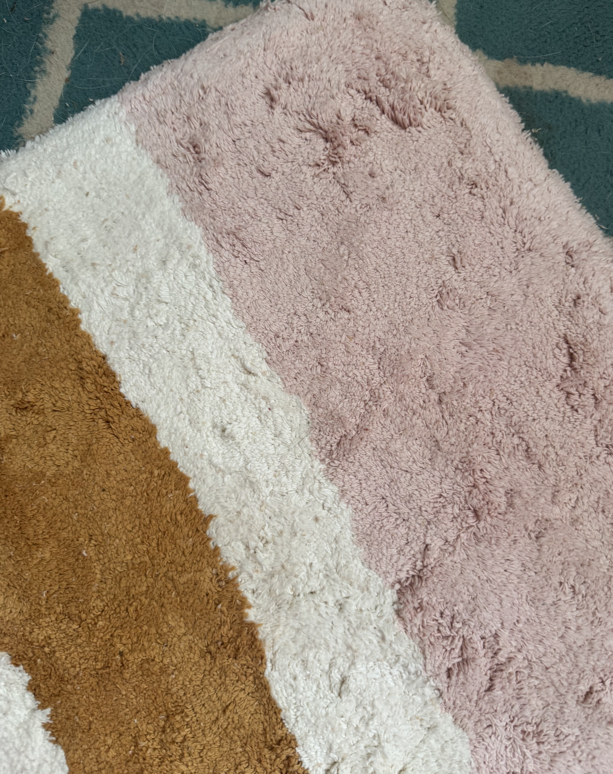 A close-up of a textured rug with diagonal stripes in pink, white, and brown on top of a blue and white patterned carpet.