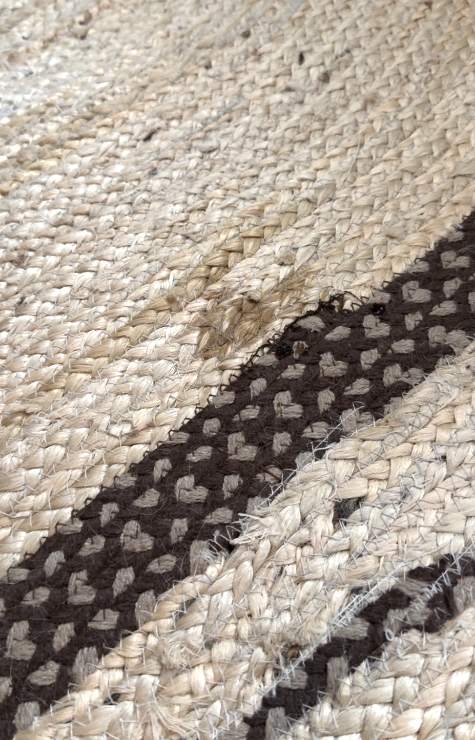 A close-up of a woven rug with tan and brown patterns, showing a frayed and damaged spot near one of the darker stripes.