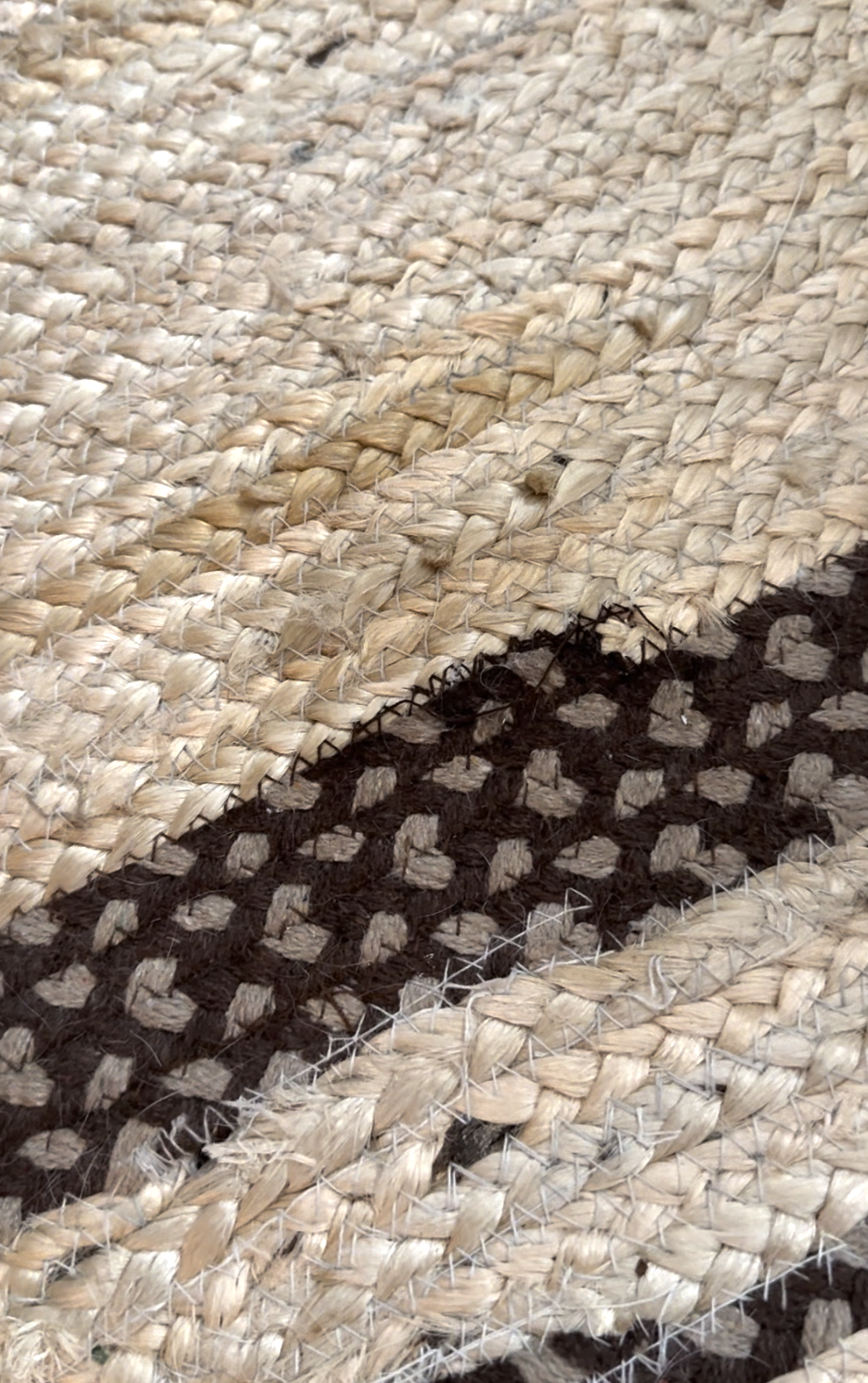 Close-up of a woven straw mat with a black and brown dotted pattern on a natural beige background.