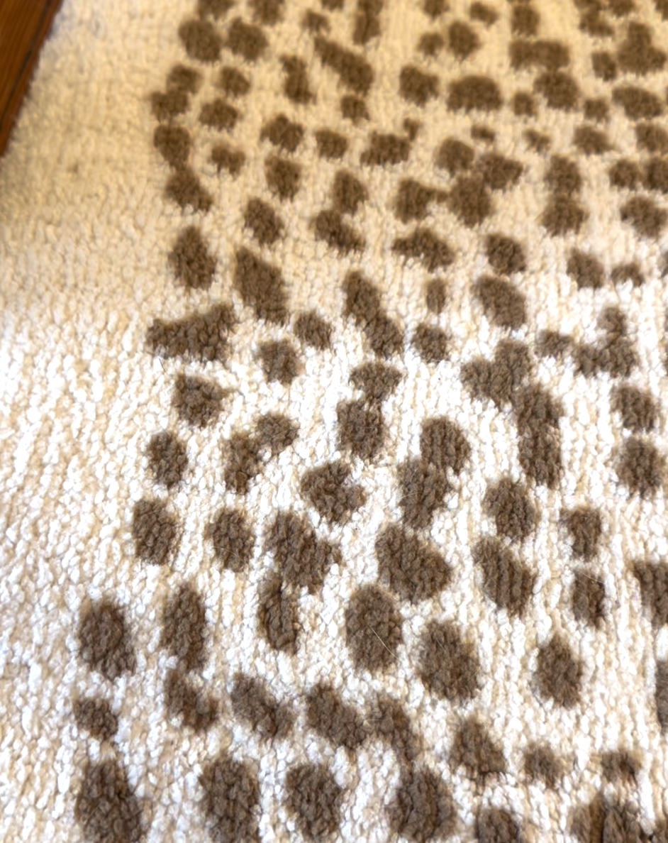 Close-up of a textured rug with a cream background and irregular brown spots, resembling an animal print pattern.