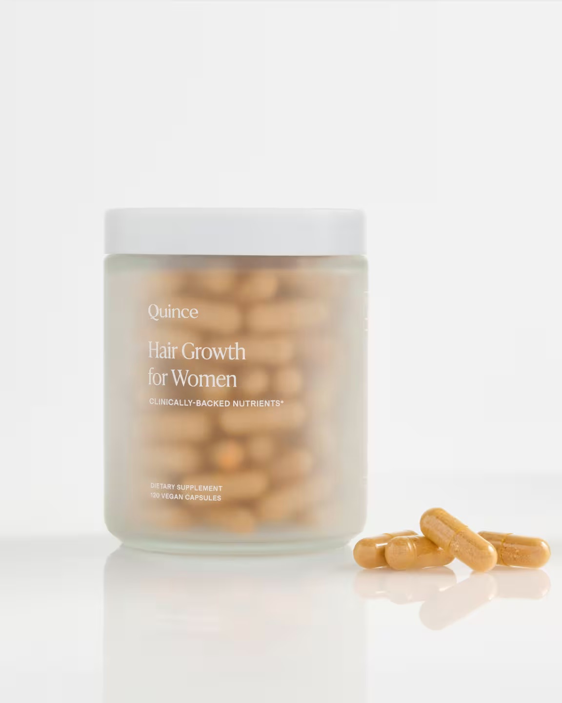 A clear jar labeled “Hair Growth for Women” contains brown capsules, with a few capsules lying in front of the jar on a white surface.