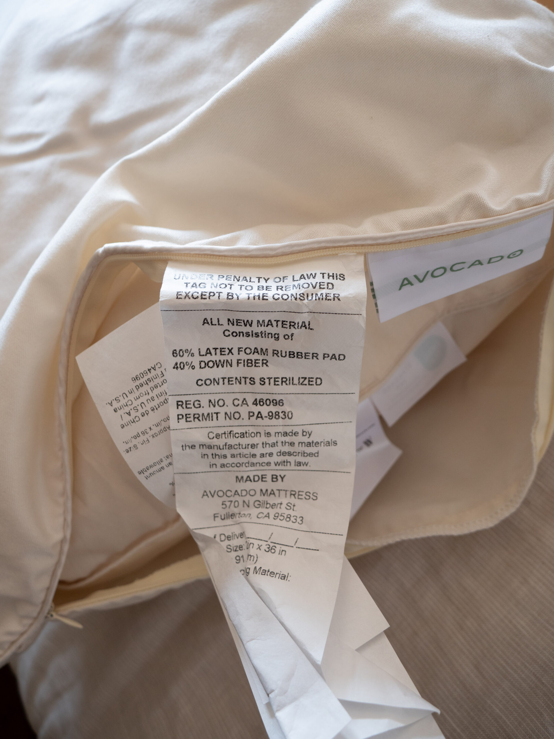 Close-up of a mattress tag showing material details—60% latex from rubber pad, 40% down fiber—plus manufacturer and legal information, partially pulled from a mattress case.
