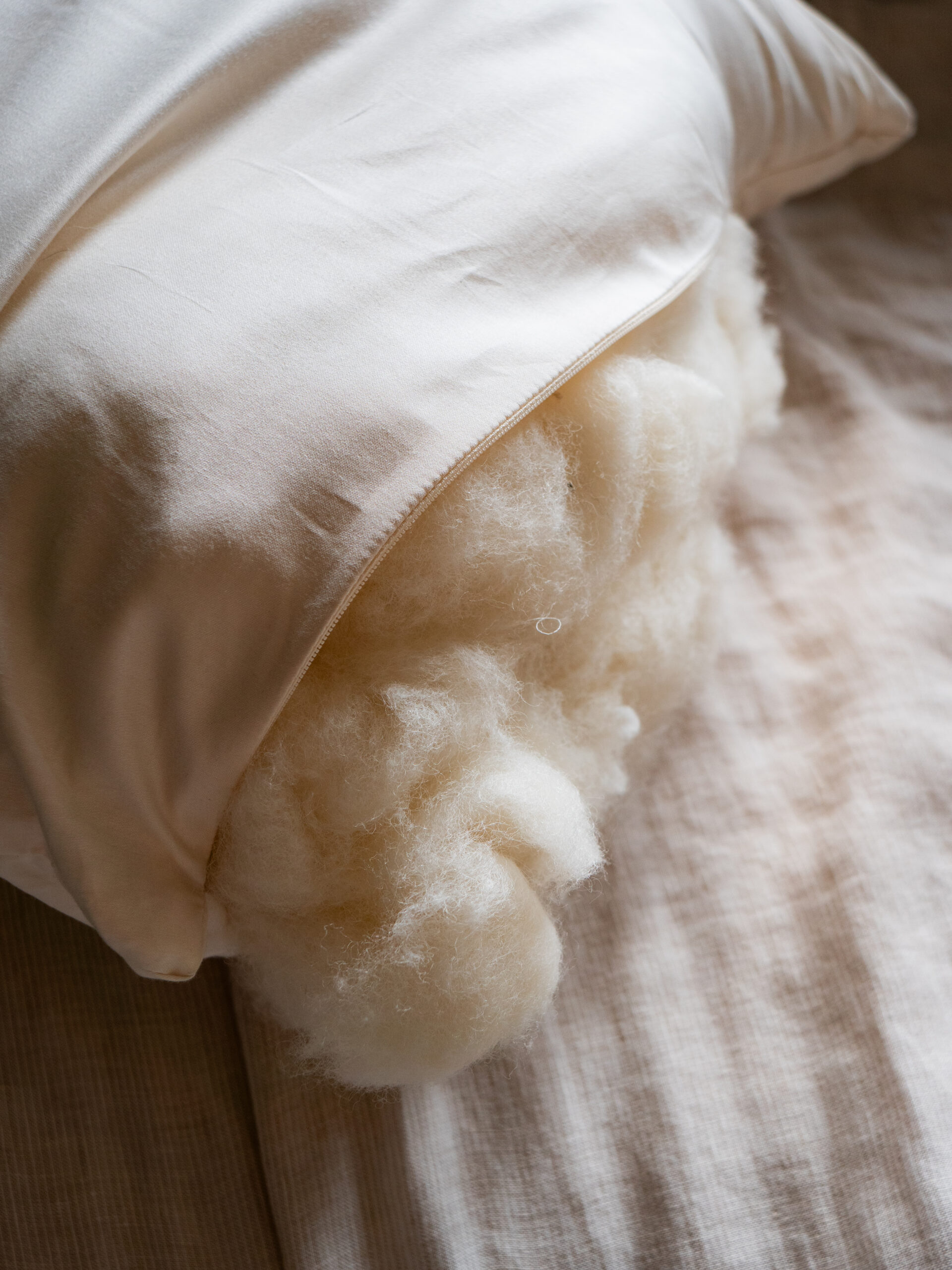 A white pillow with its cover partially open, showing fluffy filling spilling out onto a beige fabric surface.