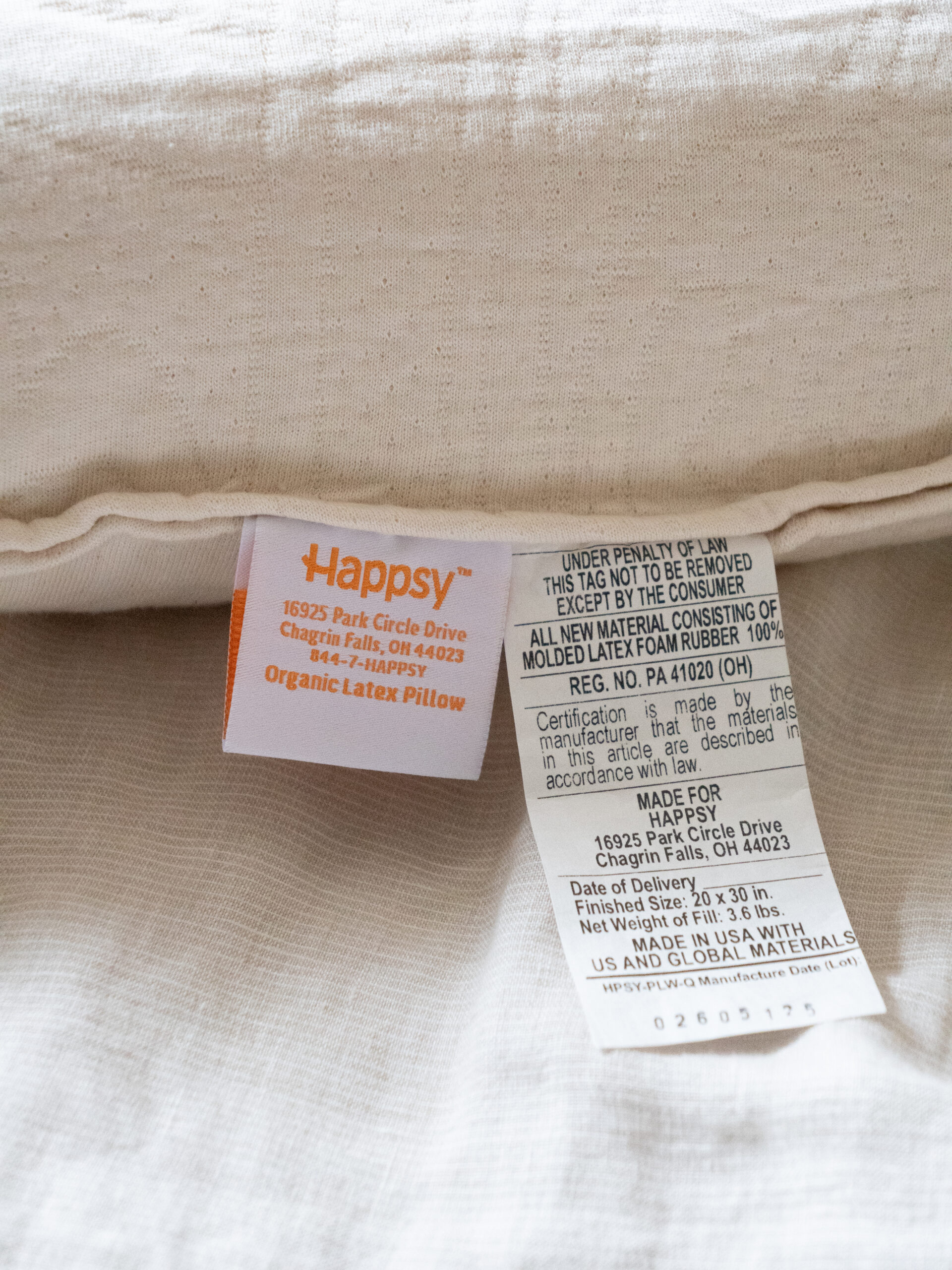 Close-up of two tags on a pillow, one with the brand name "Happpy" and address, and another detailing materials and manufacturing information.