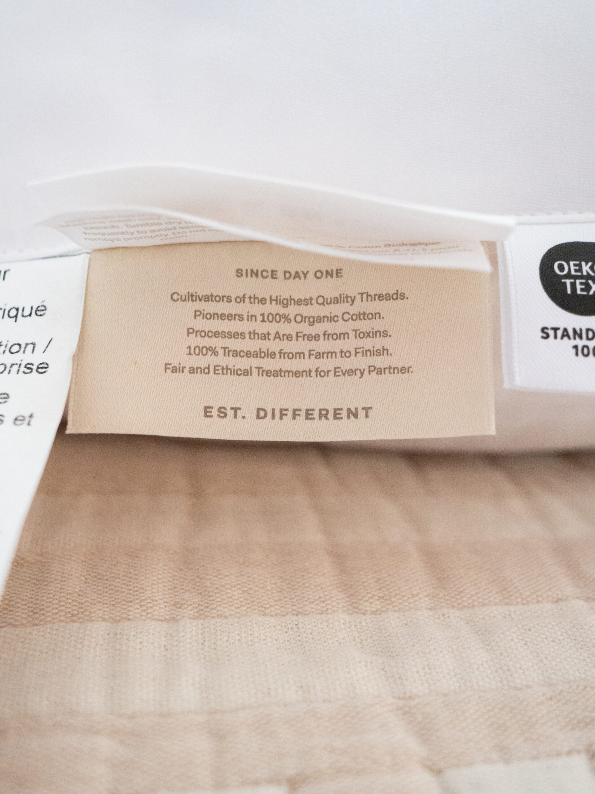 Clothing tag with text stating the use of 100% organic cotton, free from toxins, traceable from farm to finish, and ethical treatment for partners.