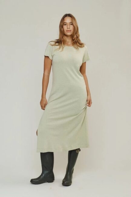A woman wearing a short-sleeve, light-colored midi dress and black boots stands facing forward against a plain background.