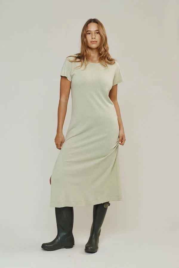 A woman wearing a short-sleeve, light-colored midi dress and black boots stands facing forward against a plain background.