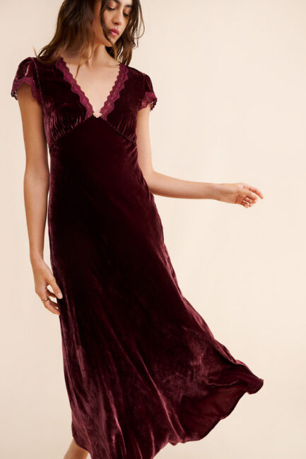 A person wearing a burgundy velvet midi dress with lace trim and cap sleeves.