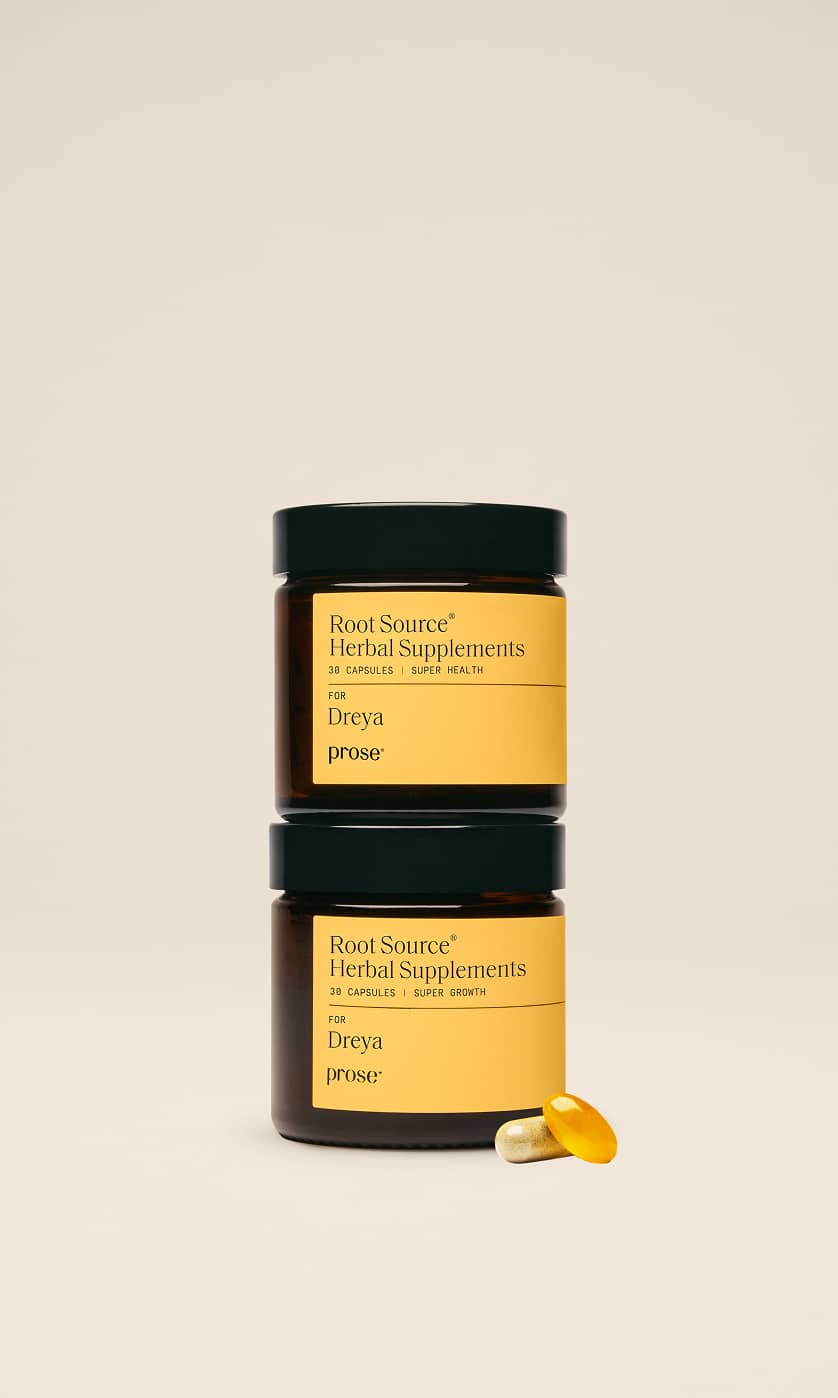Two stacked brown jars labeled “Root Source Herbal Supplements,” with yellow labels, next to a yellow capsule and a clear capsule, set against a plain beige background.