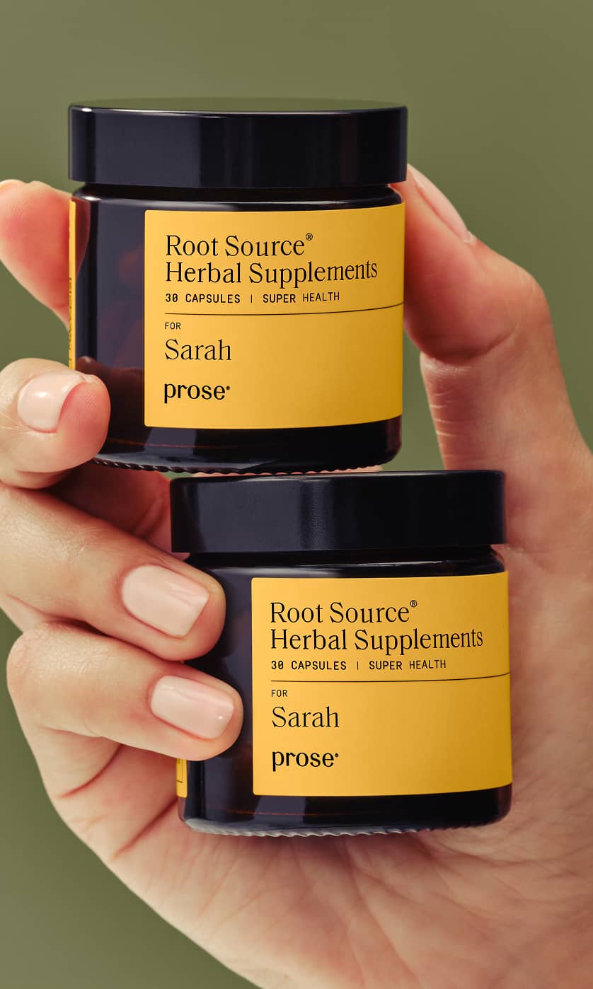 A hand holds two amber jars labeled “Root Source Herbal Supplements for Sarah” by Prose, each containing 30 capsules, against a green background.
