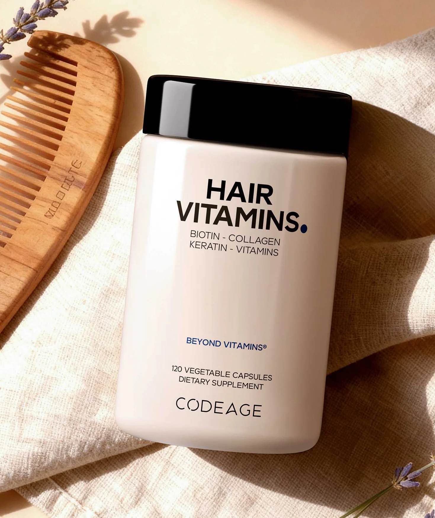 A bottle of Codeage Hair Vitamins sits on a beige cloth next to a wooden comb, with sunlight casting soft shadows across the scene.