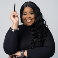 Woman with long black hair, wearing a black top, holds a pen up and smiles at the camera against a plain light background.