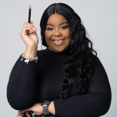 Woman with long black hair, wearing a black top, holds a pen up and smiles at the camera against a plain light background.