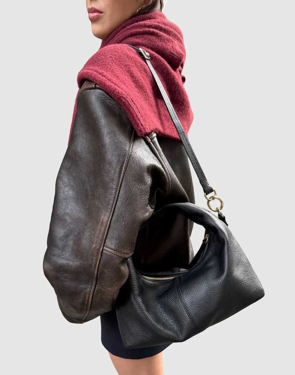 A person wearing a brown leather jacket and a maroon hoodie carries a black leather hobo bag.