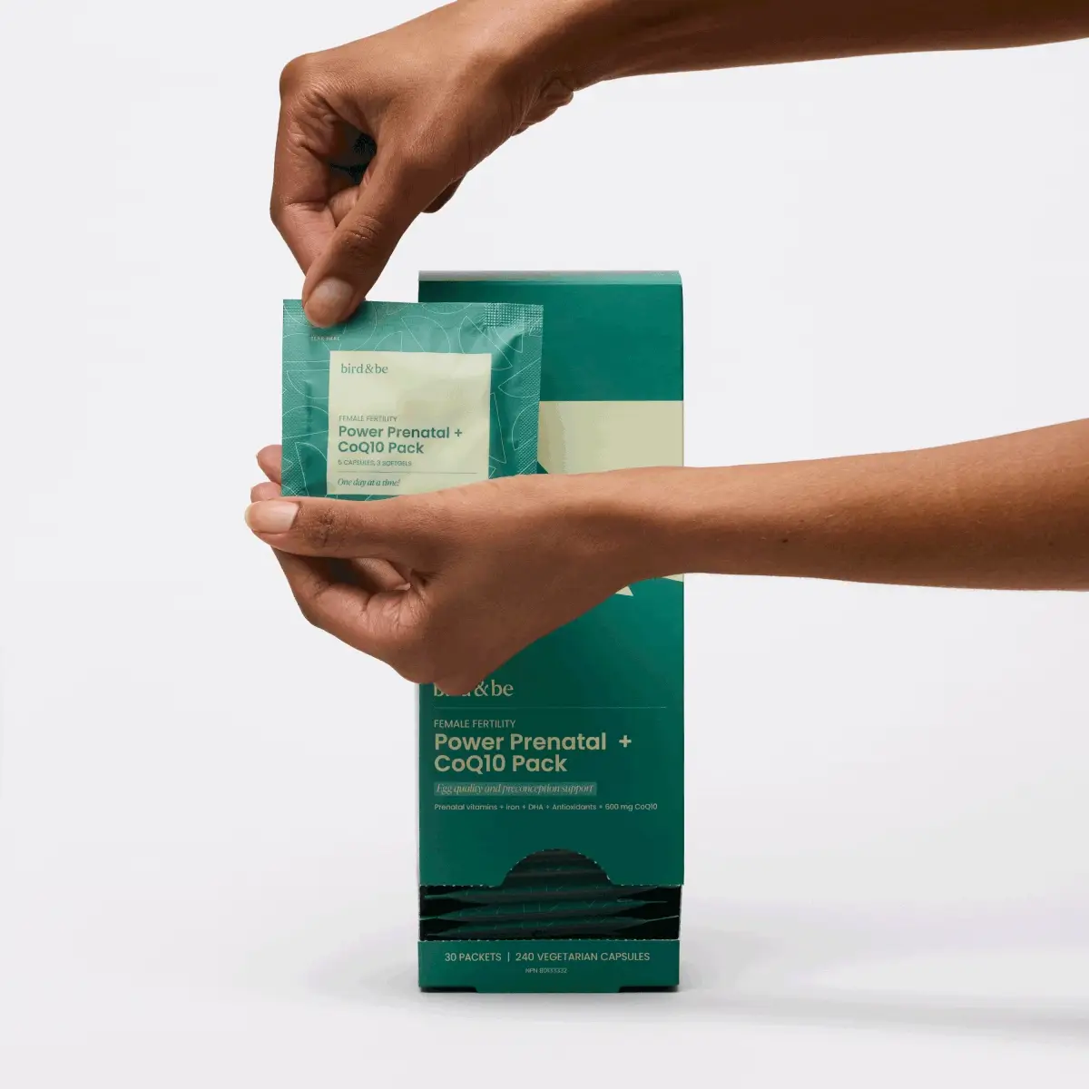 A person holds a small green packet labeled “Power Prenatal + CoQ10 Pack” in front of a matching product box on a plain background.