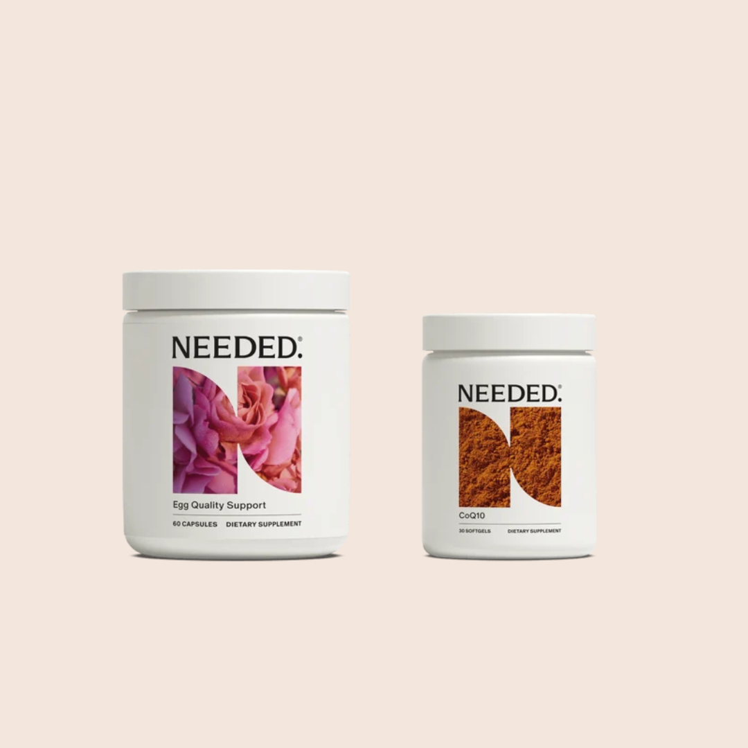 Two white supplement containers labeled “NEEDED.” The left jar has a pink rose image and says “Egg Quality Support,” while the right jar says “CoQ10” with an abstract orange design.