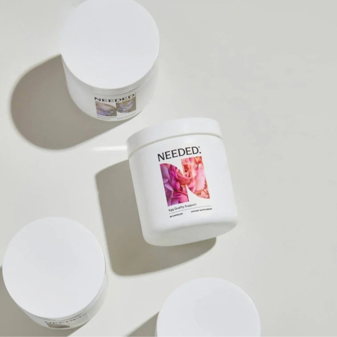 Four white tubs with white lids, one labeled “NEEDED. Egg Quality Support” featuring a floral image, are arranged on a light surface.