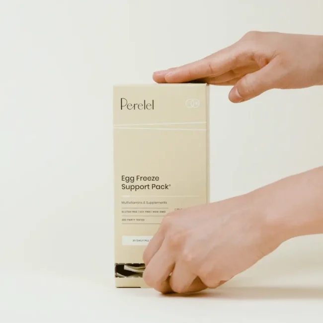 A person opens a beige box labeled “Perelel Egg Freeze Support Pack” multivitamin and supplement. The background is plain and light-colored.