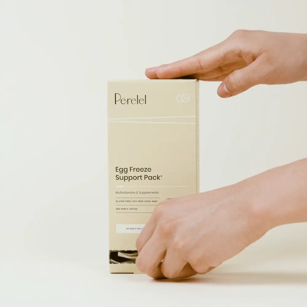 A person opens a beige box labeled “Perelel Egg Freeze Support Pack” multivitamin and supplement. The background is plain and light-colored.