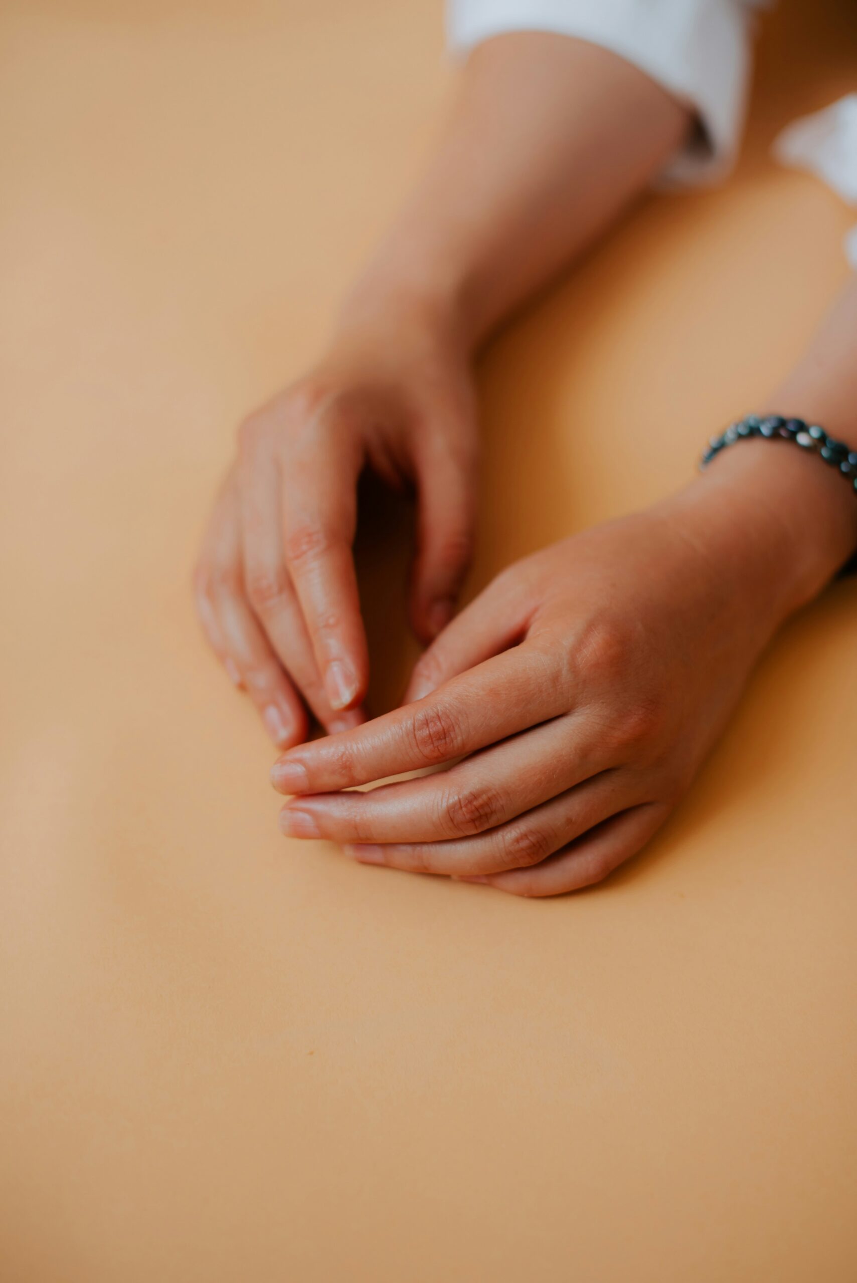 Two hands resting on a light beige surface, with one wrist wearing a beaded bracelet.