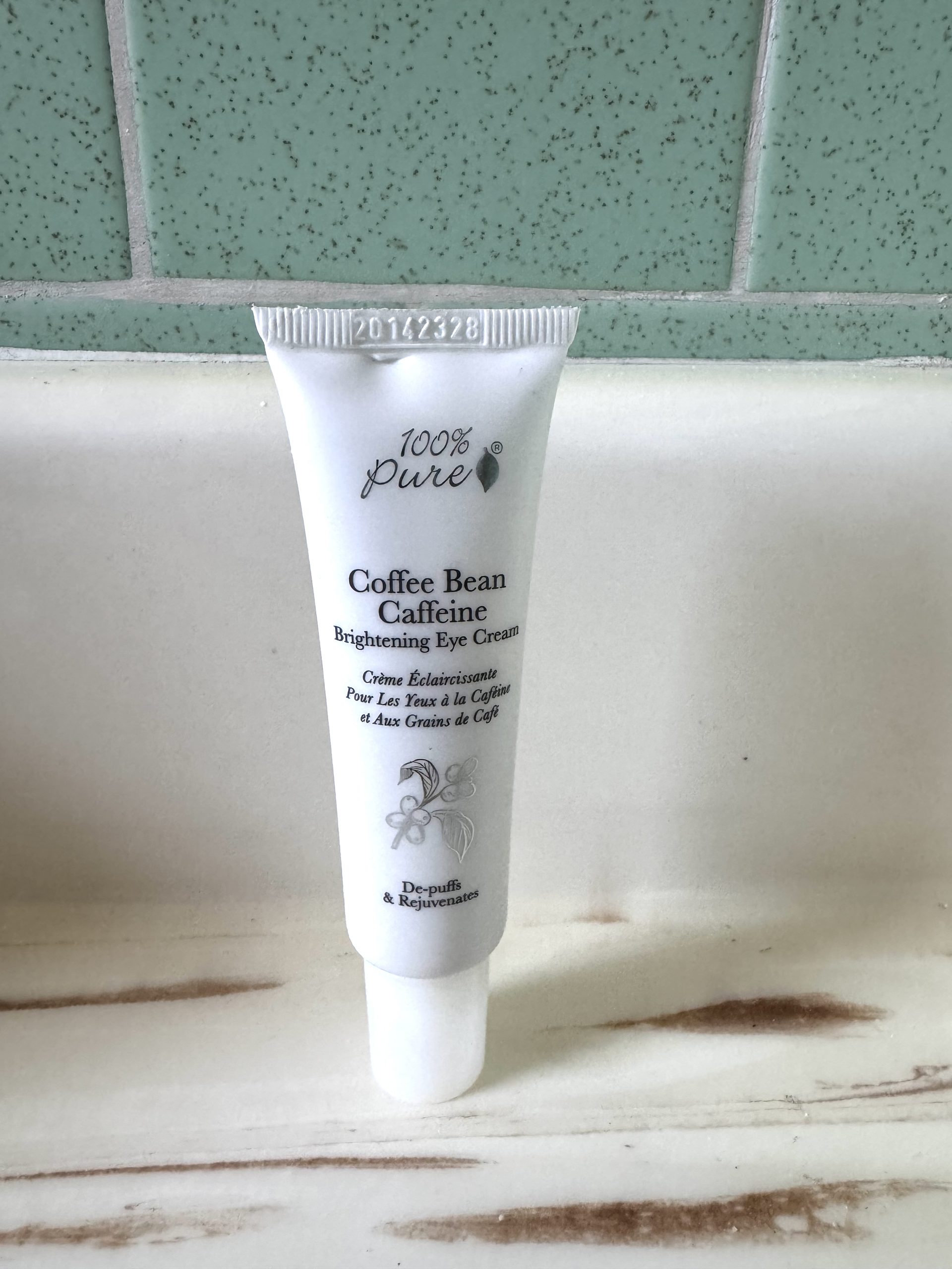 A white tube of 100% Pure Coffee Bean Caffeine Brightening Eye Cream standing on a bathroom counter.