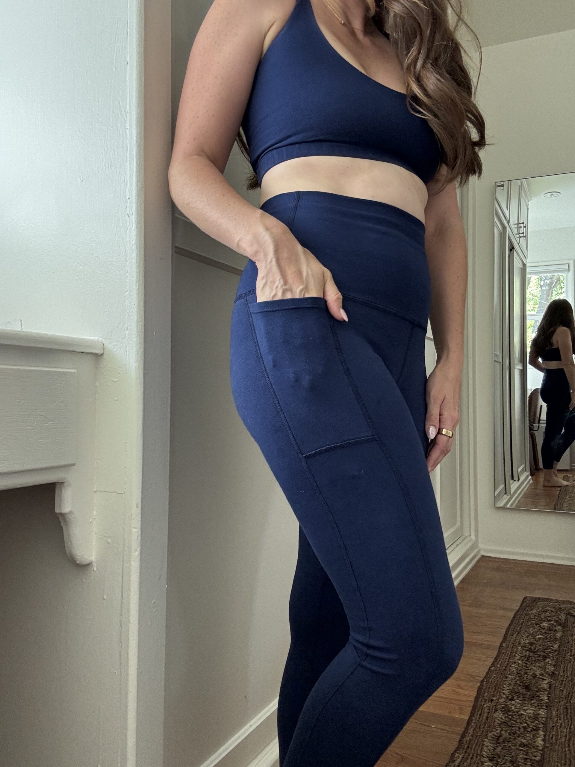 A person wearing a navy blue sports bra and high-waisted leggings with a side pocket.